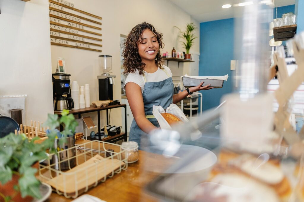 Woman smiling while working in a coffee shop and holding pastries.