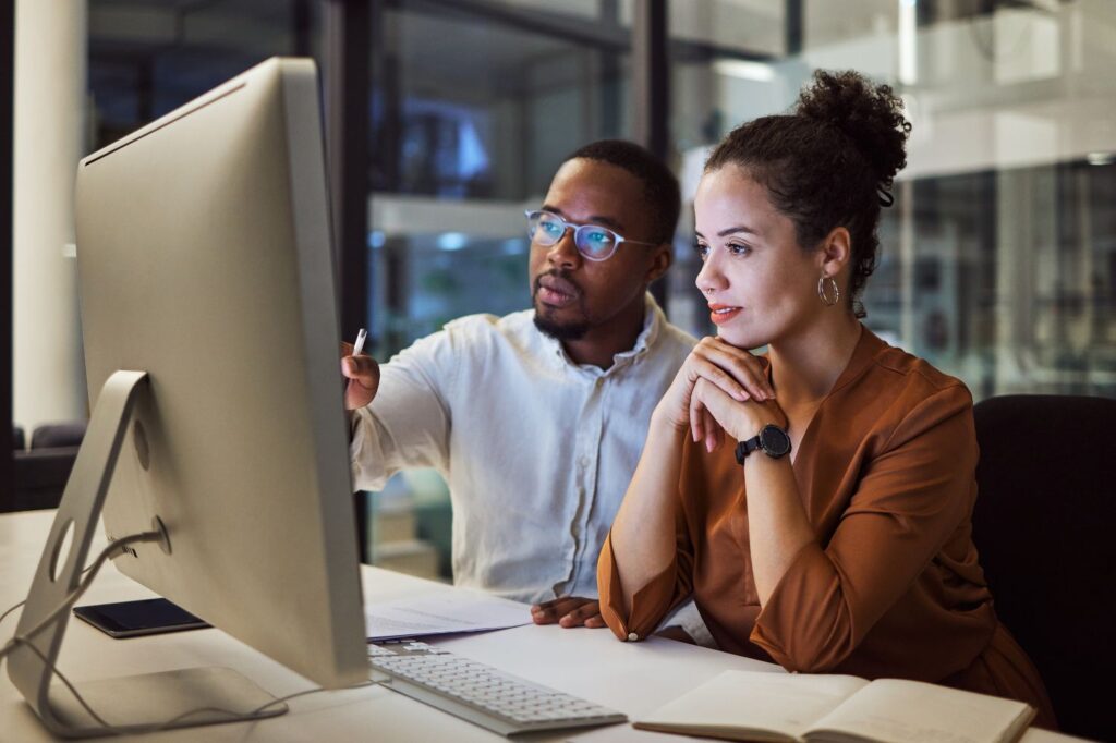 Man and woman sitting at a desk together and looking at a computer screen.