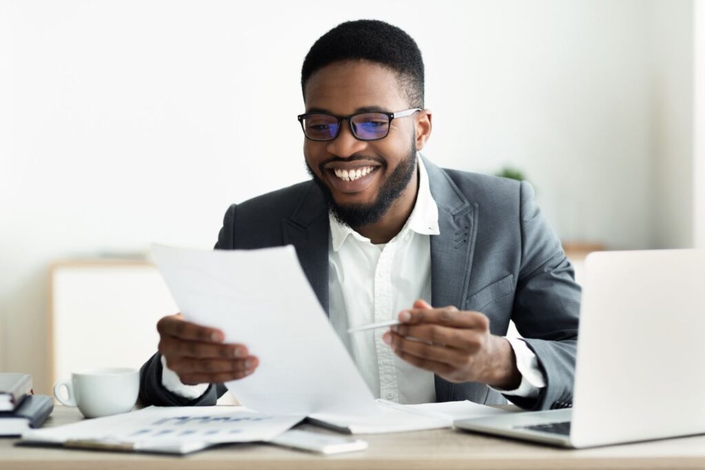Businessman smiling while looking over a report as he's sitting at his desk.